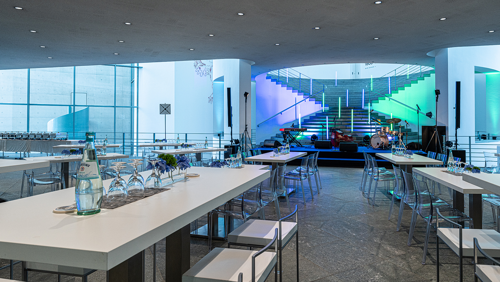 Blick in die modern illuminierte Eventlocation mit Bühne, Bar und Sitzbereichen