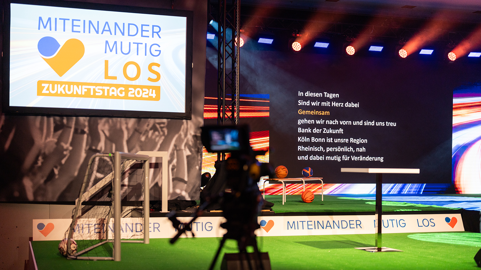 Bühne mit LED-Leinwand, darauf das Motto des Zukunftstags und ein lyrischer Text