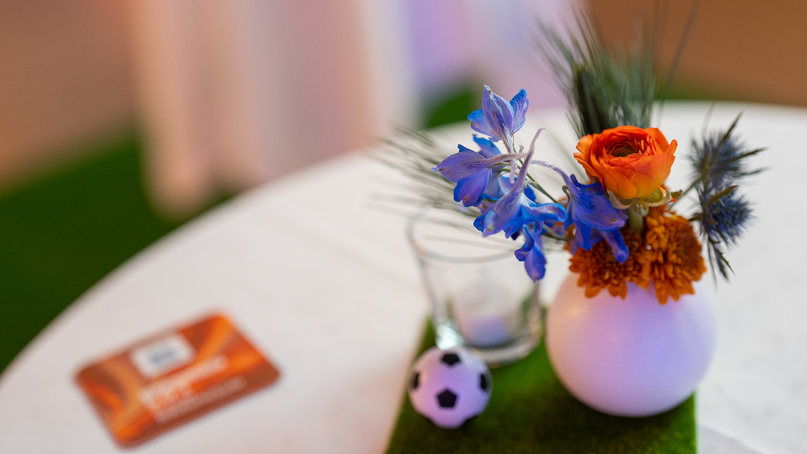 Tischdekoration mit oranger Blume, blauen Akzenten und Mini-Fußball
